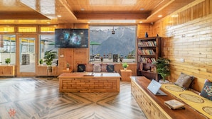 A cozy, wooden-themed interior with a central seating area, a bookshelf, and a TV screen. - Zostel Kalpa (Kalpa)