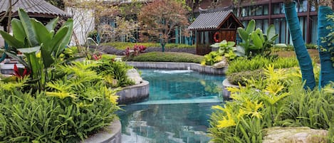 A landscaped pool area with tropical plants and a traditional building in the background.