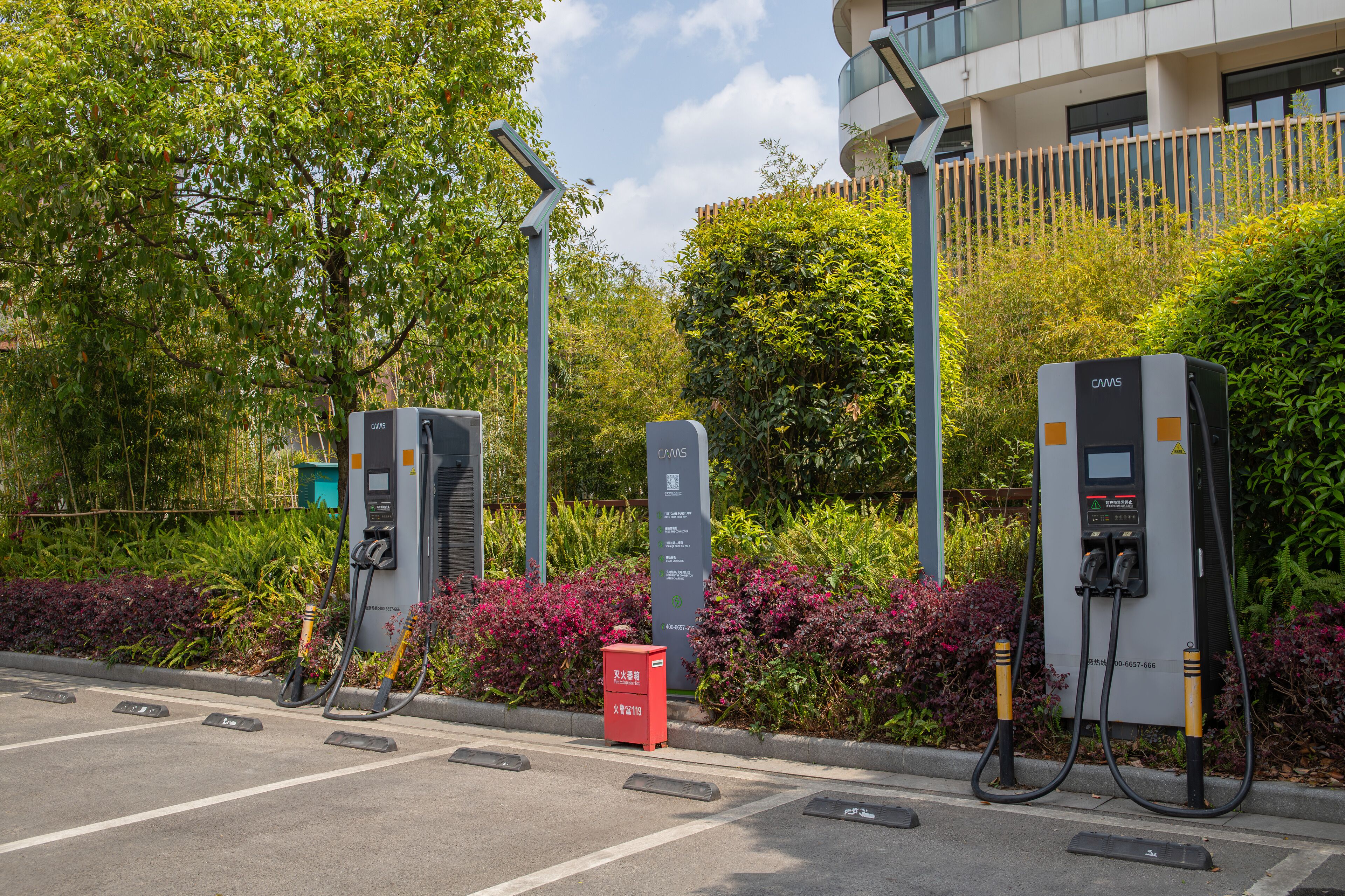 A parking area with electric vehicle charging stations, a red mailbox, and a building with a modern design in the background.