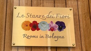 Une enseigne sur fond en bois portant les inscriptions « Le Stanze dei Fiori » et « Rooms in Bologna ».