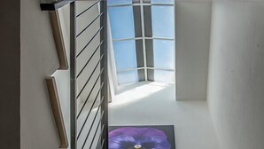 Un escalier avec une rampe en métal menant à une pièce dotée d’une grande fenêtre et d’un tableau représentant des fleurs, encadré.