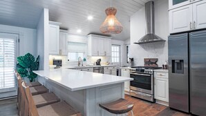 A modern kitchen with white cabinetry, a large island with bar stools, stainless steel appliances, and a hanging light fixture.