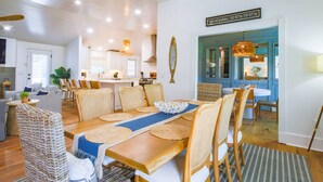A spacious dining area with a wooden table and wicker chairs, a kitchen in the background, and a sign indicating the location.