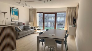 Un salon moderne avec un canapé, une table à manger et une grande fenêtre donnant sur un immeuble.