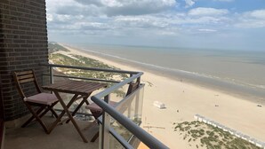 A balcony with a wooden table and chairs, overlooking a beach with sand and water. - Apartment near Port with Scenic Views (Nieuwpoort)