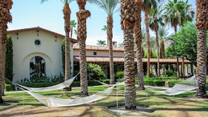 A courtyard with palm trees, a white building with a red-tiled roof, and two hammocks. - Setting the Standard by AvantStay | Luxury Villa (La Quinta)