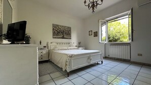 A bedroom with a bed, dresser, TV, and a window with a view of trees.