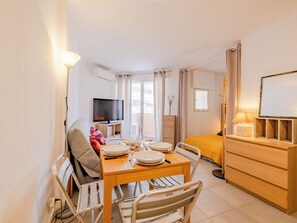 Quarto de hotel pequeno com área de refeições, uma cama, televisão e mesa de cabeceira com abajur.