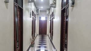 A hotel hallway with a checkered floor, air conditioning units, and wooden doors. - Hotel O P&g Guest House (Medan)