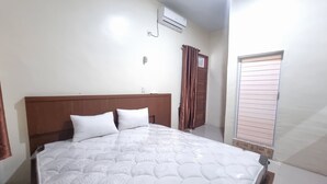 A bedroom with a large bed, a wooden headboard, an air conditioning unit, a window with blinds, and a door with curtains. - Hotel O P&g Guest House (Medan)