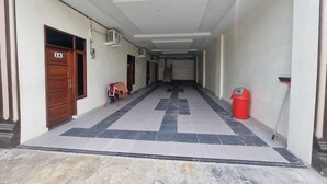 A hallway with a tiled floor, a wooden door labeled "IA", and a red trash bin. - Hotel O P&g Guest House (Medan)