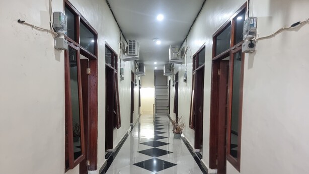 A hallway with a black and white checkered floor, air conditioning units mounted on the walls, and wooden doors. - Hotel O P&g Guest House (Medan)