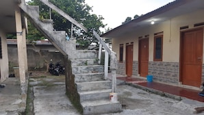 Um edifício com uma escadaria de concreto que leva a uma porta, uma motocicleta estacionada e um balde azul no chão.