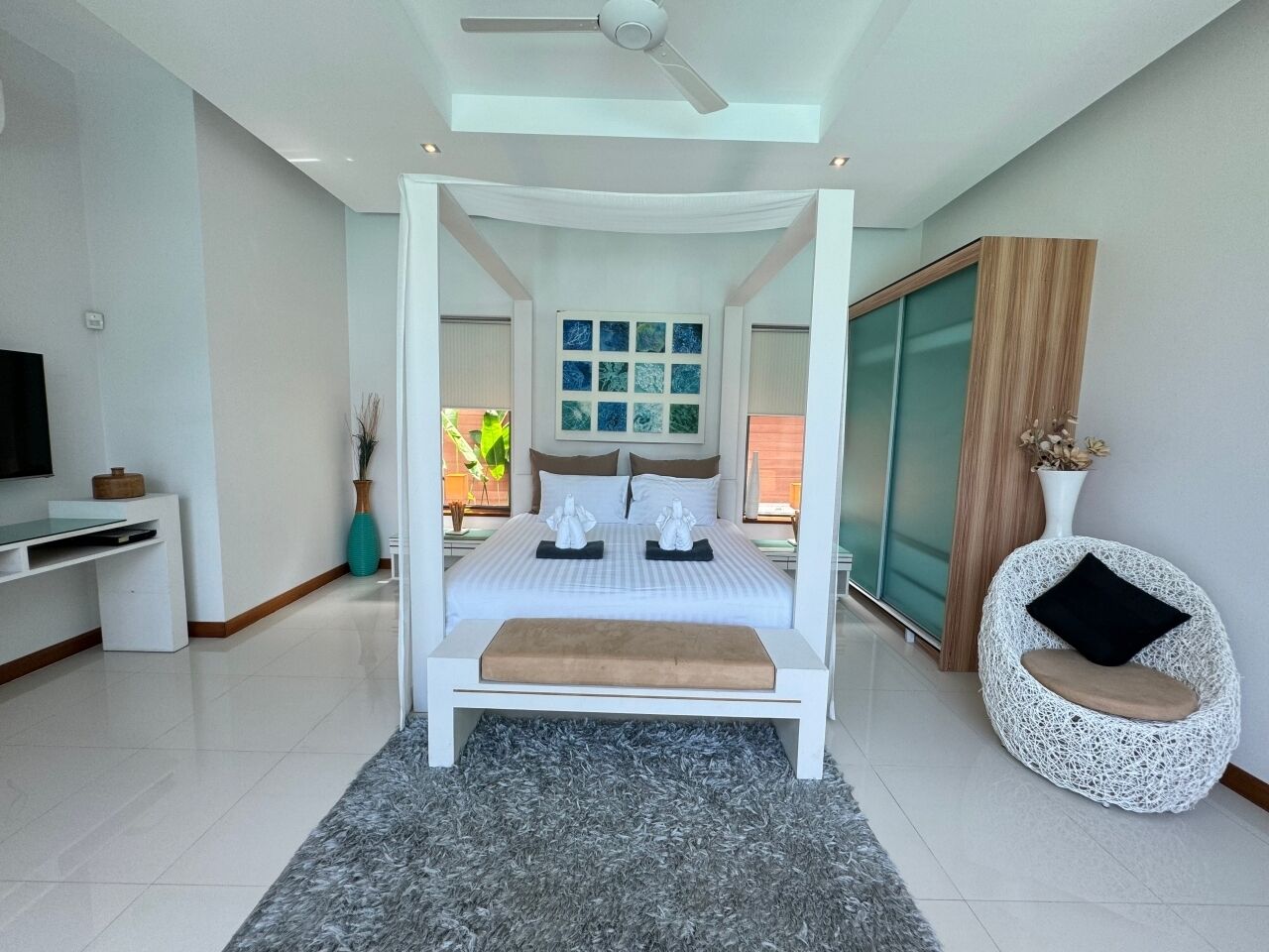 Une chambre à coucher moderne avec un lit à baldaquin, un téléviseur à écran plat, un bureau et un fauteuil décoratif.