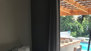 A bedroom with a bed, a pillow with a decorative design, a window with a view of a pool and outdoor furniture. - 28 La Rochelle Bed & Breakfast (Kimberley)