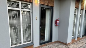A building with a number '5' on the wall, a fire extinguisher mounted on the wall, and a window with a metal grille. - 28 La Rochelle Bed & Breakfast (Kimberley)