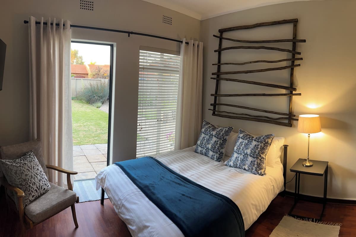 Un dormitorio con cama, una silla, un televisor, una lámpara y una ventana con persianas.