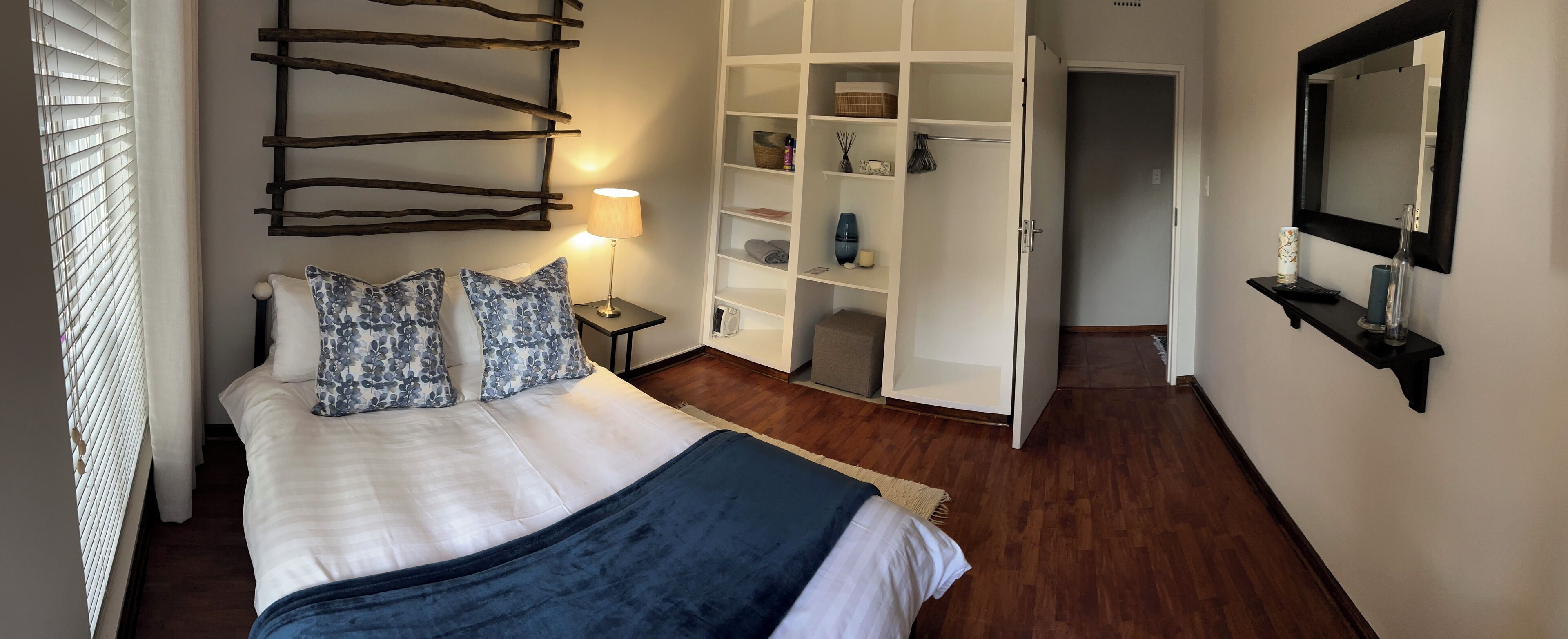 Un lit bien fait, agrémenté de coussins à motifs floraux, une lampe de chevet et une armoire avec des étagères.