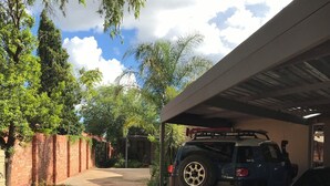 A paved driveway leading to a covered parking area with a brick wall and greenery on one side. - 28 La Rochelle Bed & Breakfast (Kimberley)