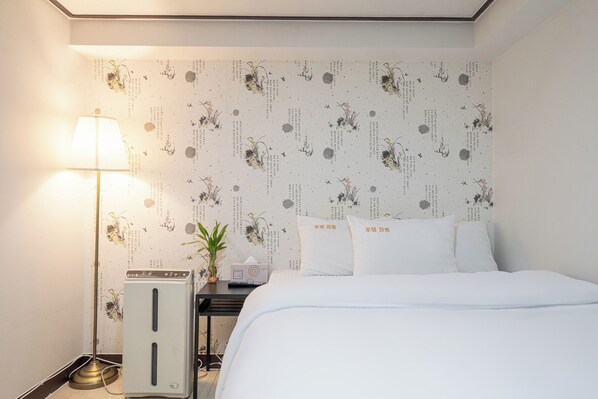 Ett hotellrum med en säng, ett sängbord med en lampa, en liten växt och en dekorativ vägg med text och bilder.
