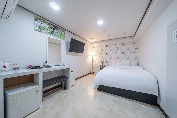 A hotel room with a bed, a desk with a computer, a TV mounted on the wall, and a lamp.