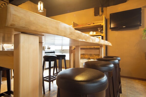 A bar area with stools, a wooden counter, and a television mounted on the wall.