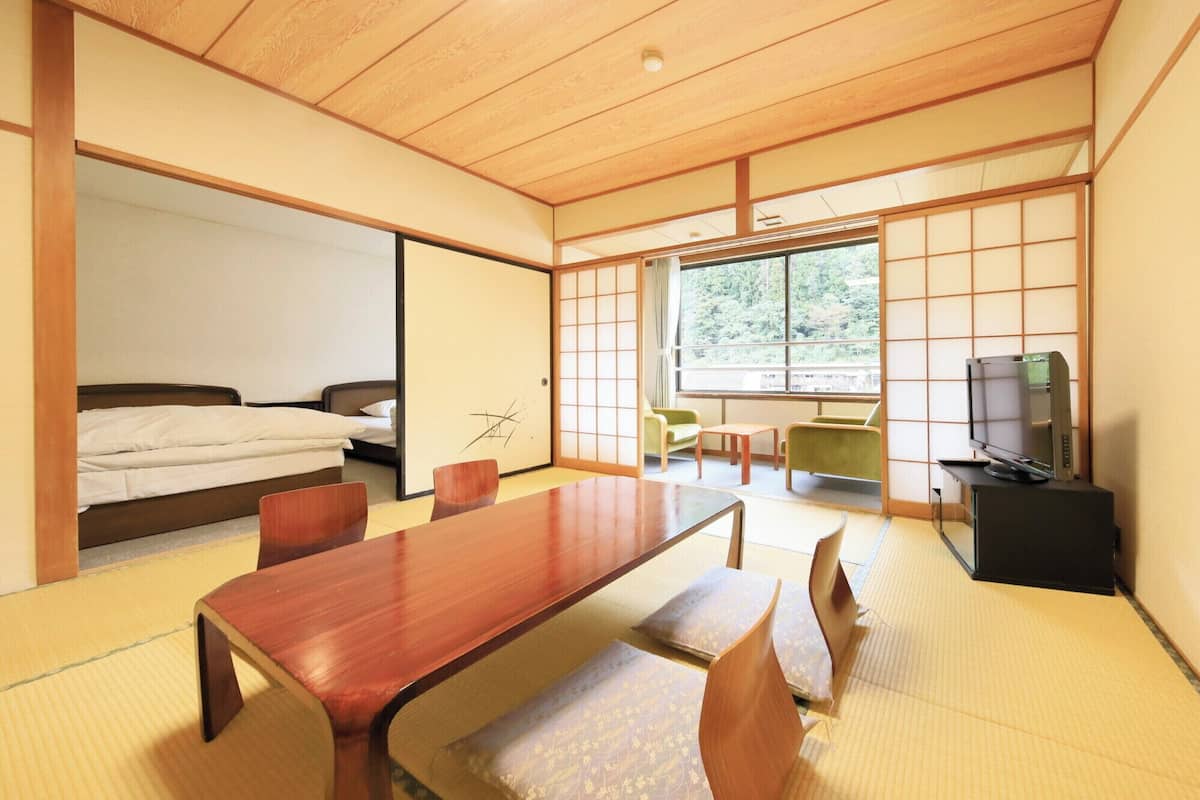 A traditional Japanese-style room with tatami flooring, a low wooden table, and a bed with a futon.