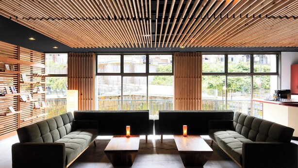 A modern interior with a wooden slatted ceiling, large windows, and a seating area with sofas and tables.