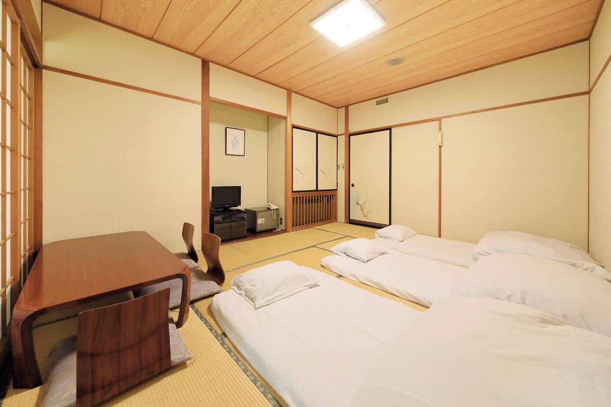 A traditional Japanese room with tatami flooring, a low wooden desk, a television, and a futon bed.