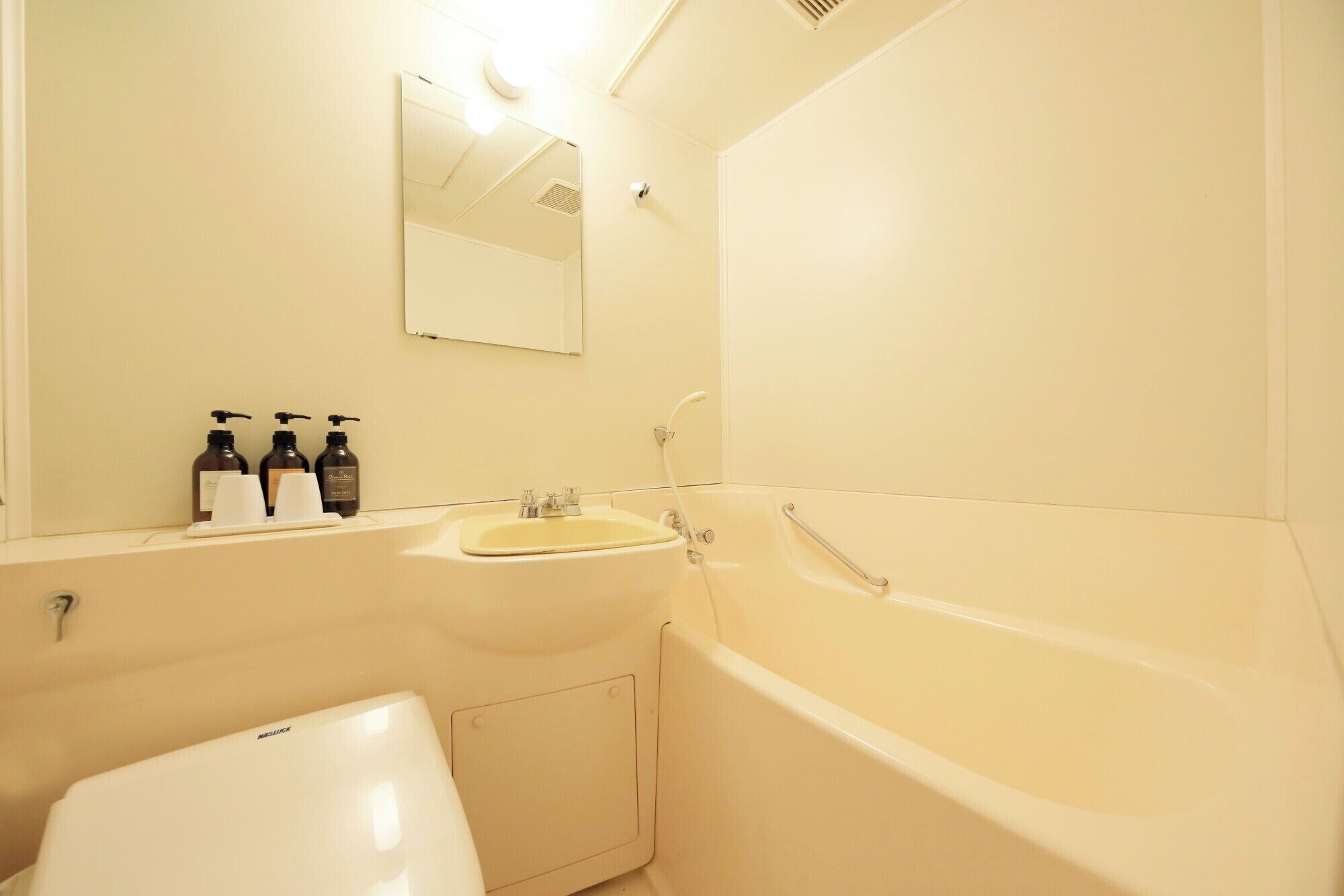 A bathroom with a sink, mirror, and bathtub. There are toiletries on the sink counter.