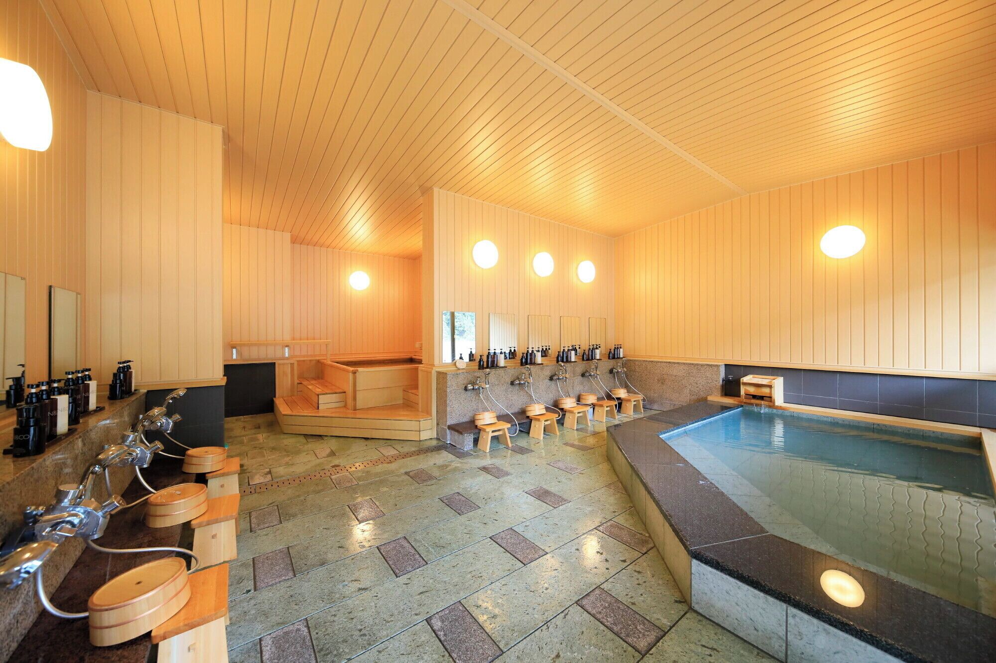 A sauna with wooden benches, a central hot tub, and multiple sinks with bottles.
