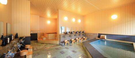 A sauna with wooden benches, a central hot tub, and multiple sinks with bottles.
