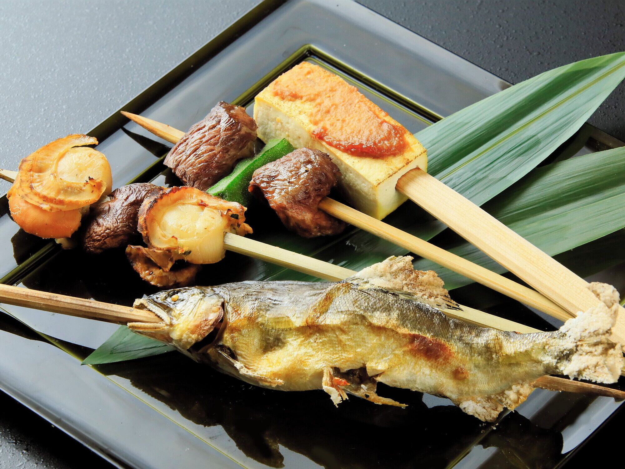 Diversos pinchos de comida, incluyendo pescado, carne y verduras, sobre un plato.