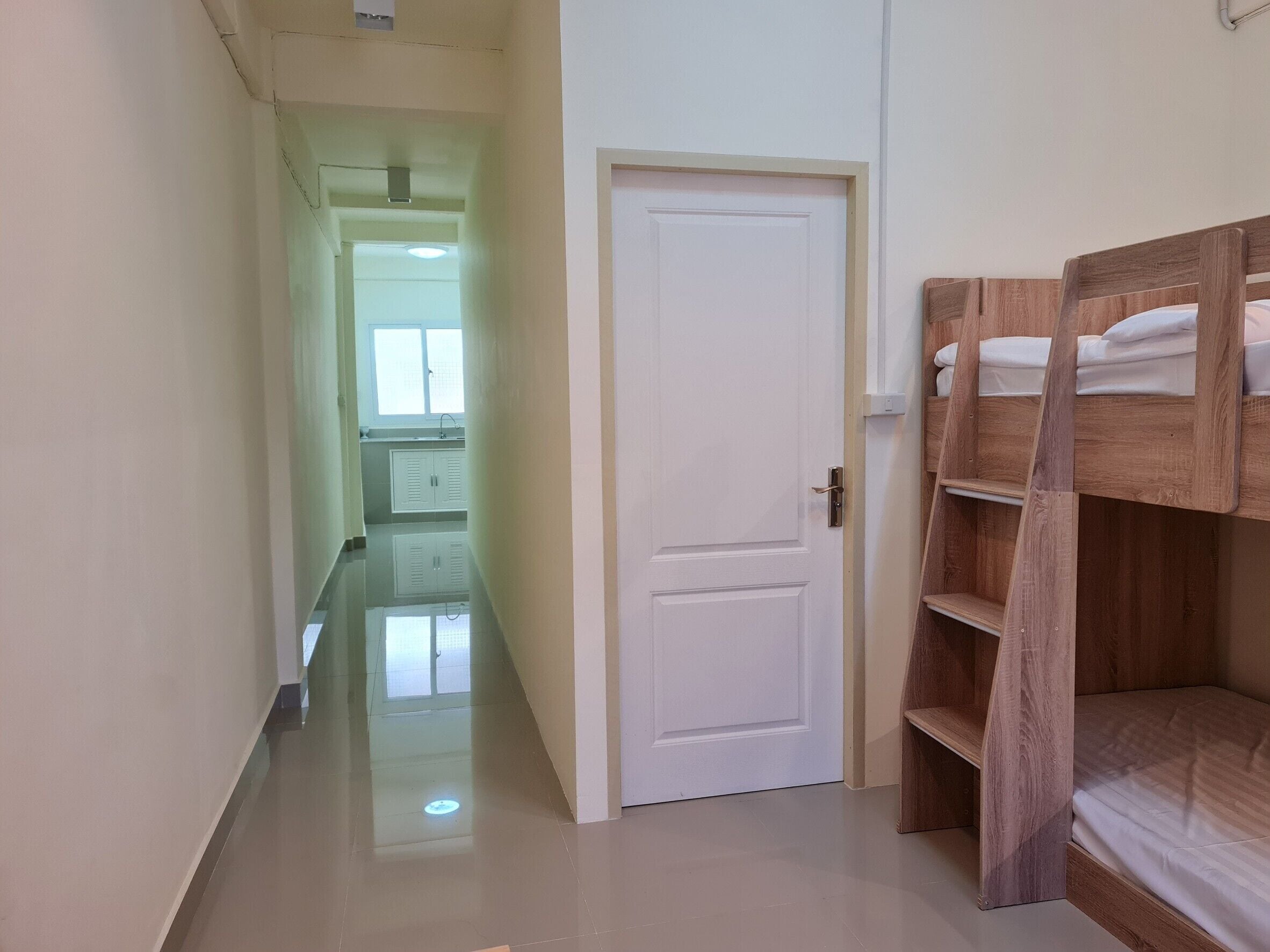 Un corridoio stretto che porta a una stanza con un letto a castello e una porta bianca.