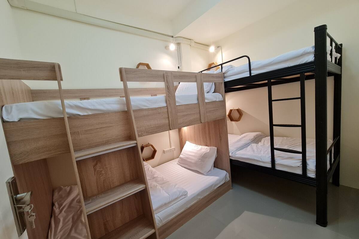 A bunk bed room with wooden and black bunk beds, a wooden ladder, and a hexagonal light fixture.