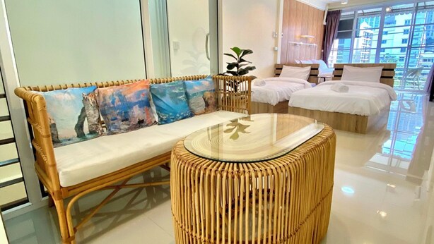 A modern hotel room with a glass partition, a wicker sofa, a round table, and a bed with a wooden headboard. - De Chalet (Bangkok)