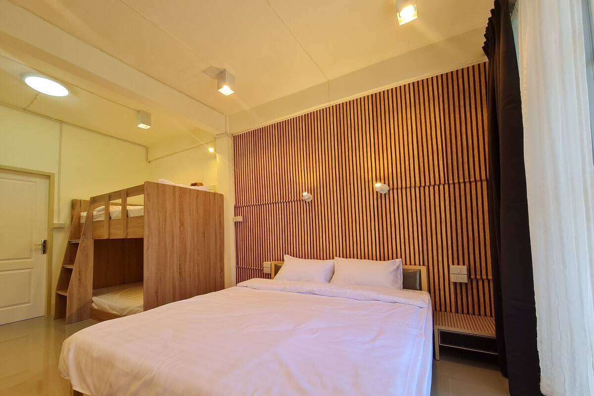 A bedroom with a bunk bed, a single bed, wooden paneling on the wall, and a door.