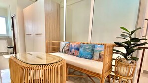 A modern interior with a round wicker table, a cushioned bench with colorful cushions, and a potted plant. - De Chalet (Bangkok)