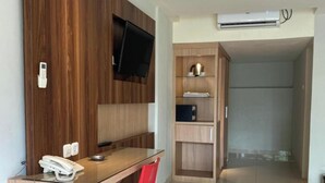 Egy modern szállodai szoba, melyben van egy fa íróasztal, egy piros szék, egy falra szerelt, síkképernyős televízió, egy minibár, és egy előtér, amely egy másik szobába vezet.