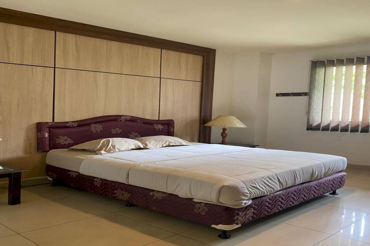 A bedroom with a bed, a nightstand, a lamp, and a window with blinds.