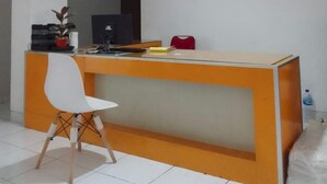 A reception desk with a white chair, a small potted plant, a black monitor, and a red bag. - OYO 94106 Kitarooms Property (Curug)