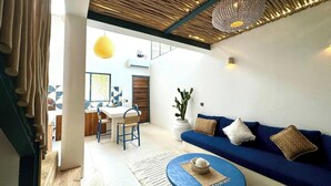 Una sala de estar moderna con un sofá azul, una mesa de centro redonda y un comedor con mesa y sillas.