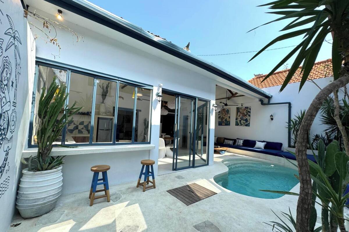 Une maison moderne dotée d’une piscine, de grandes fenêtres et d’un patio avec des tabourets.