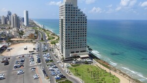 Un hôtel de grande hauteur offrant une vue sur l’océan, doté de parkings et bordé d’une route sinueuse.