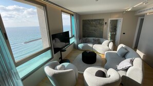 Un salon moderne doté d’une grande fenêtre donnant sur la mer, d’un téléviseur à écran plat et de meubles contemporains.