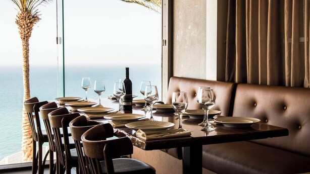 Une table à manger dressée pour six personnes, avec vue sur la mer et les palmiers.