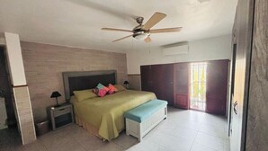 Un dormitorio con cama, mesitas de noche, un banco, ventilador de techo y vistas al exterior.