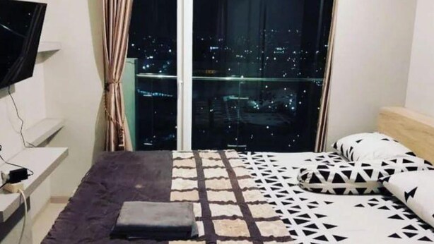 Une chambre à coucher avec un lit, un téléviseur posé sur un meuble et une vue sur la ville par une grande fenêtre.
