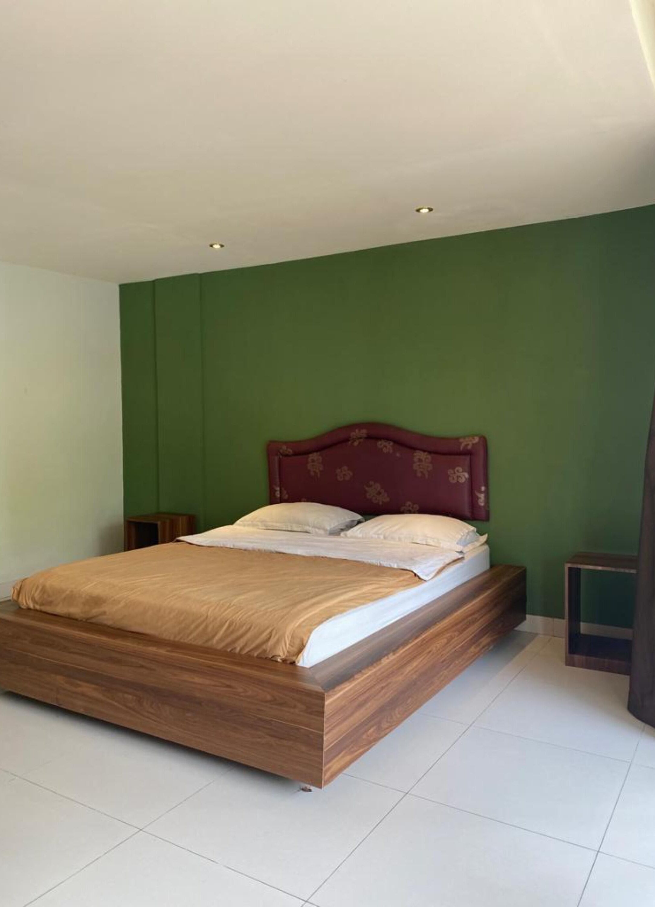 Un dormitorio con cama de madera, paredes verdes y una mesita de noche pequeña.
