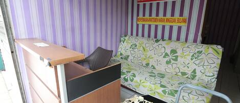Un espace d’accueil avec un bureau en bois, un banc rembourré et un canapé à motifs.